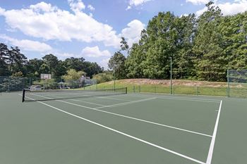 A tennis court surrounded by trees and a fence.